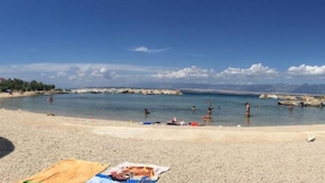 A beach with people swimming and sunbathing, a clear sky, and distant mountains. - Apartments Matković - Two Bedroom Apartment1 (Vir)