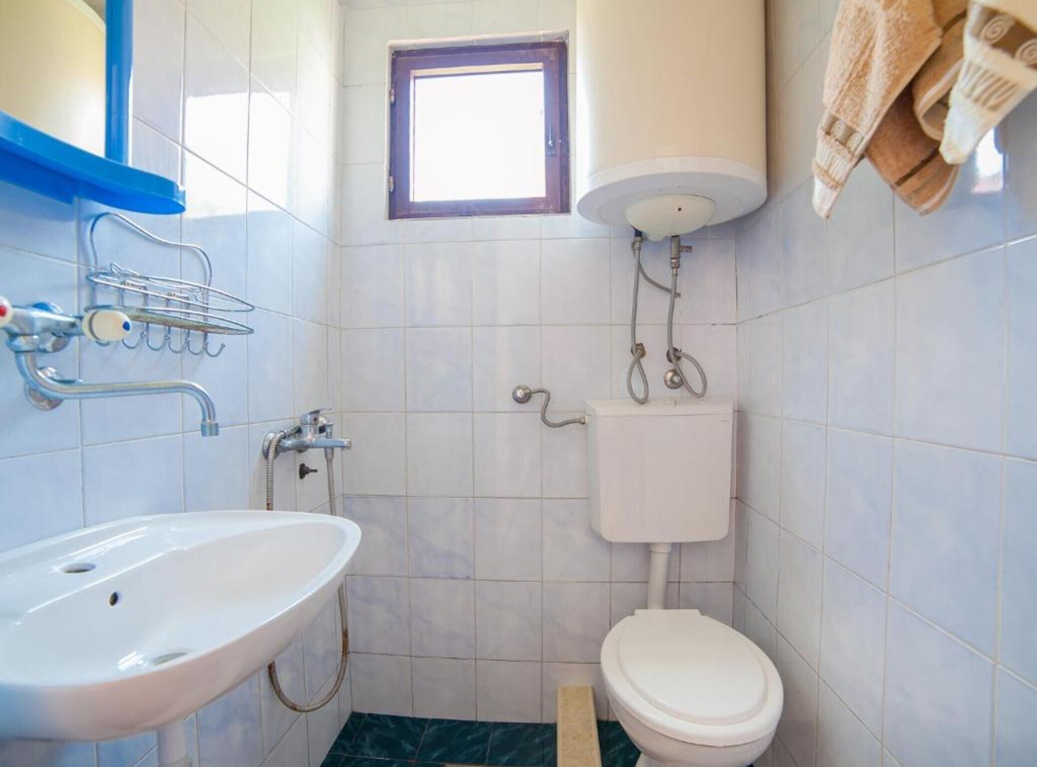Een compacte badkamer met een witte wastafel, toilet en douche. Er is een raam boven het toilet en een handdoekrek aan de muur.