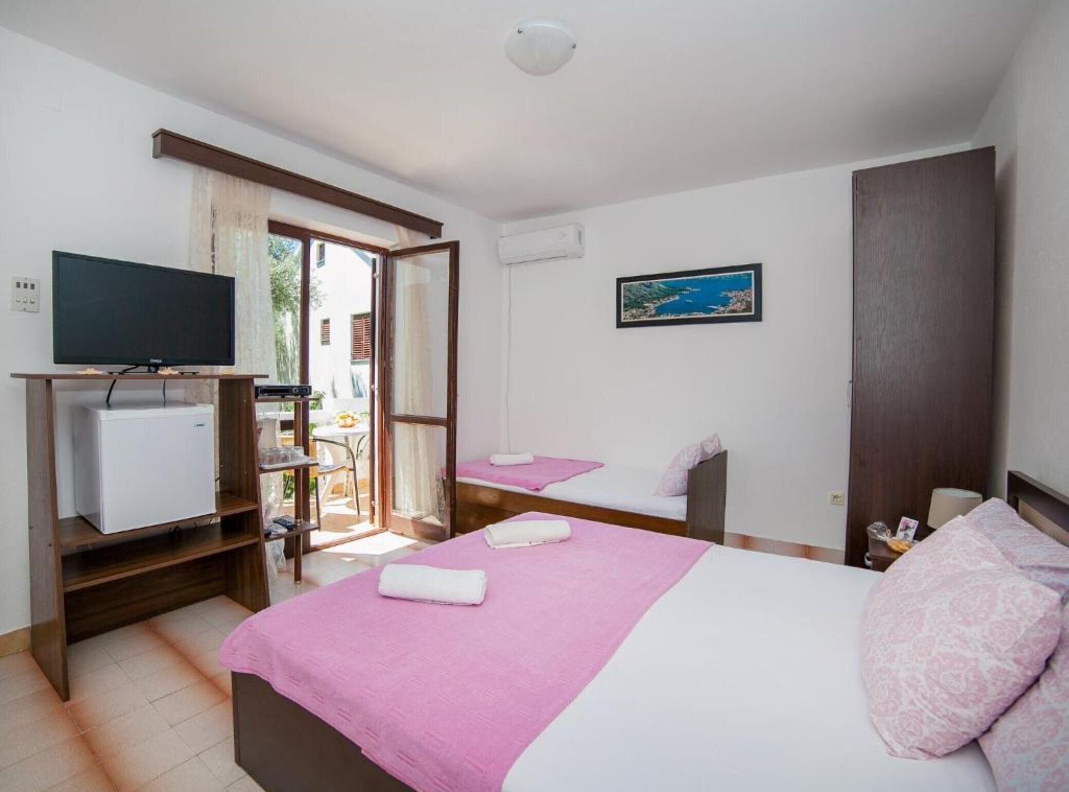 A hotel room with a bed, a TV, a small fridge, and a window with a view of the outdoors.