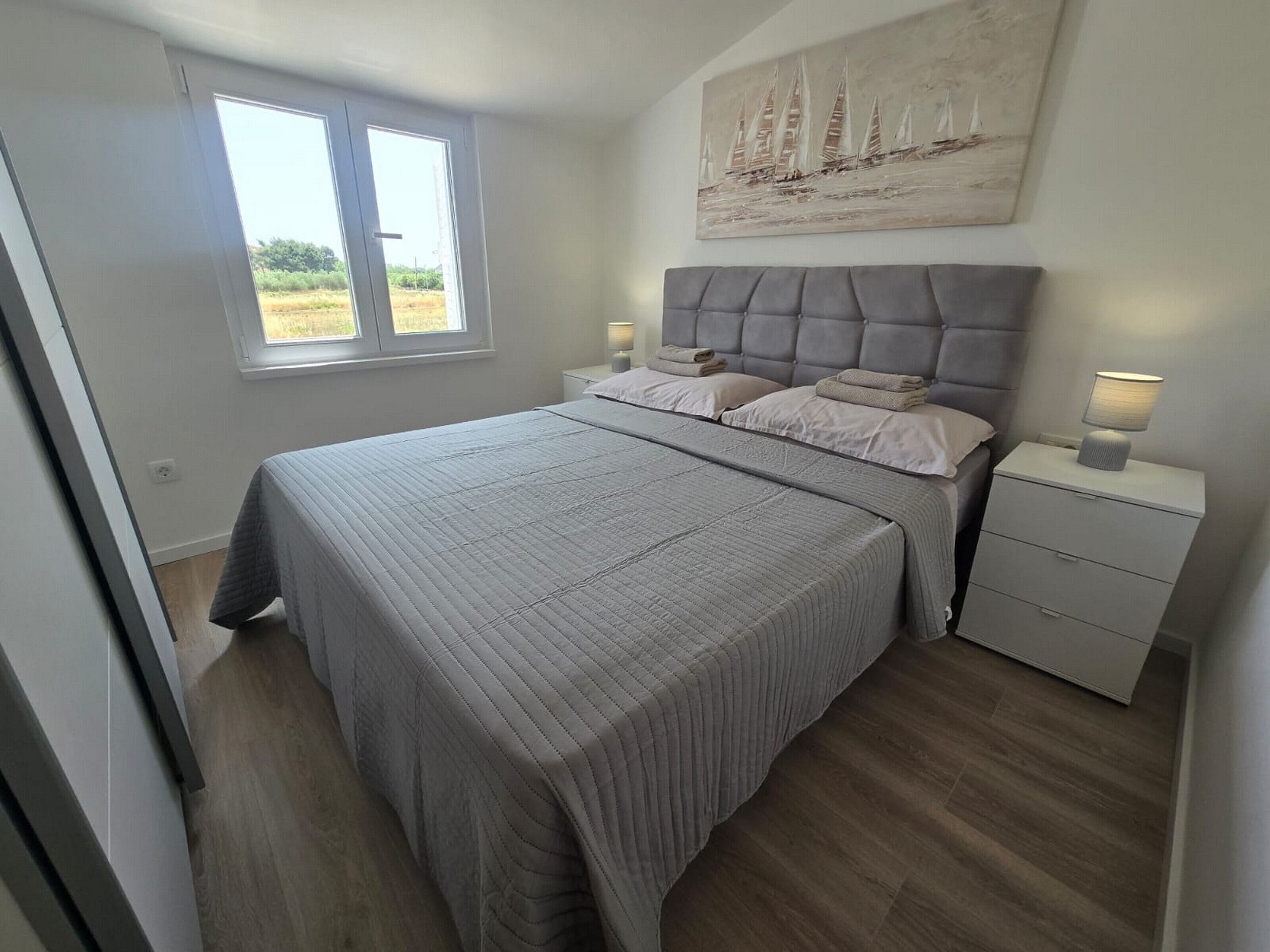 Ein Schlafzimmer mit einem großen Bett, einem Fenster, einem Nachttisch und einem Bild an der Wand.