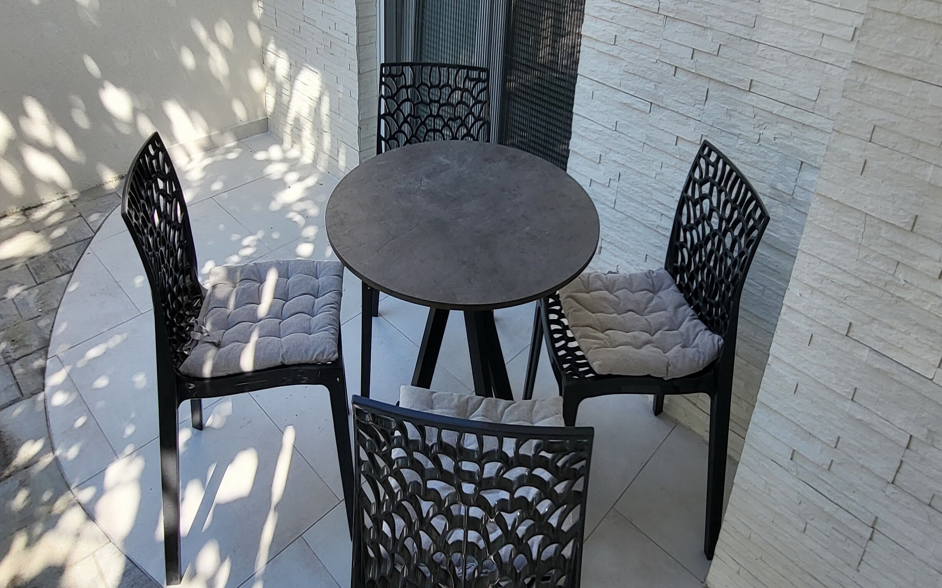 Une table ronde entourée de quatre chaises, chacune dotée d’un siège et d’un dossier rembourrés, est placée contre un mur en briques blanches.