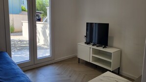 A room with a sliding glass door leading to an outdoor area, a white TV stand with a flat-screen TV, a blue sofa, and a marble table. - Apartments Ivankovic - One Bedroom Apartment with Terrace (Zaton)