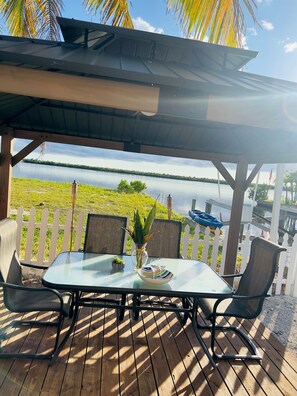 Een overdekt terras met een tafel, stoelen en uitzicht op een meer.