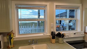 A kitchen with a double sink, a stove, and a window with a view of a fence and trees. - Fisherman's Cottage at Matlacha (Matlacha)