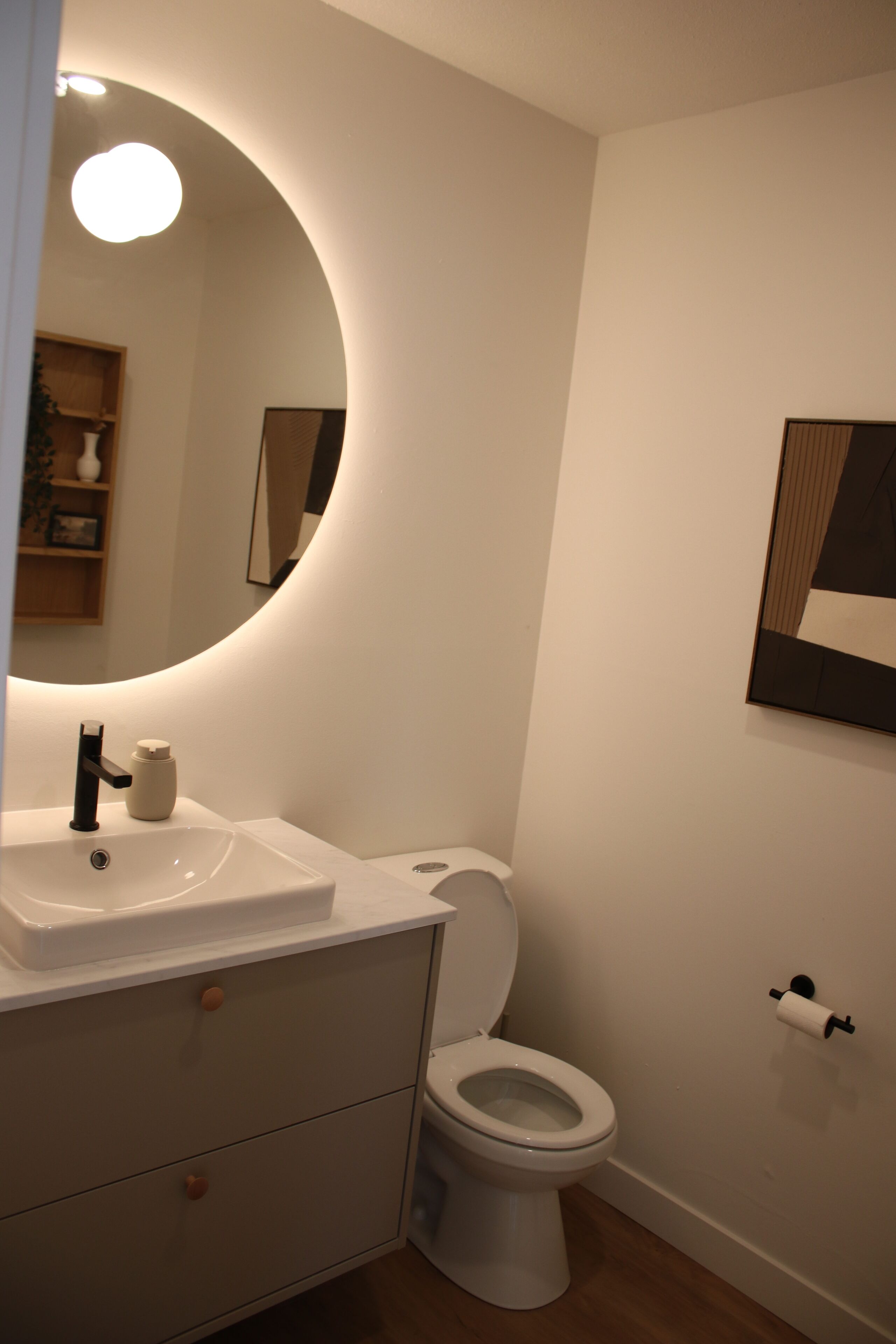 Un baño con un lavamanos blanco, un inodoro y un espejo con una luz circular encima.