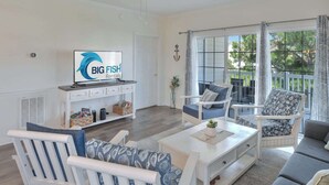 Amplia sala de estar con televisor, mobiliario blanco y vistas a través de grandes ventanales.
