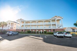 A multi-story hotel with a central courtyard, parking lot, and a clear blue sky.