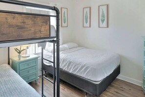 Un lit superposé avec une tête de lit en bois, une table de chevet avec une lampe et une petite table de nuit avec une plante.
