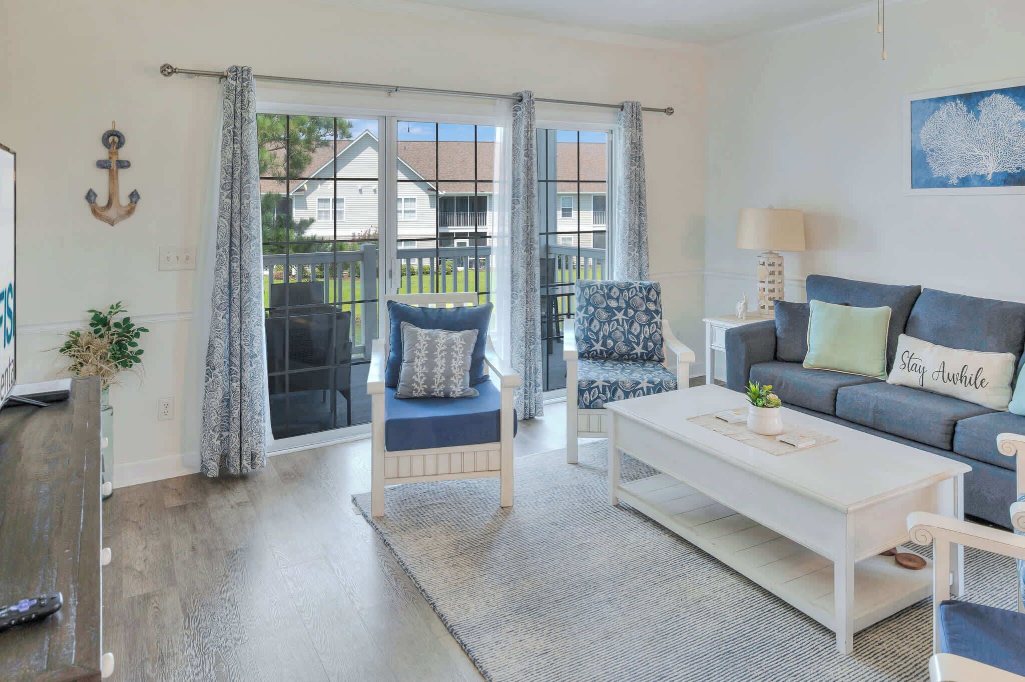 A living room with a sofa, armchair, and a coffee table. There is a sliding glass door leading to a balcony.