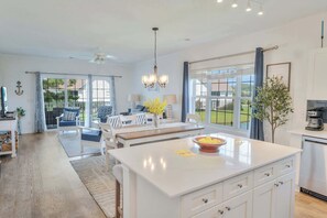 Une cuisine spacieuse avec un grand îlot central, un coin repas offrant une vue agréable et un salon doté d’un ventilateur de plafond.