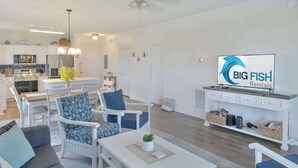 Una sala de estar moderna con comedor, muebles blancos, un televisor de pantalla plana y una cocina al fondo.