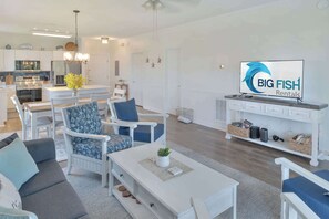 A modern living room with a dining area, white furniture, a flat-screen TV, and a kitchen in the background. - Updated Large 2BR in Azalea Lakes, Pools, PondView (Myrtle Beach)