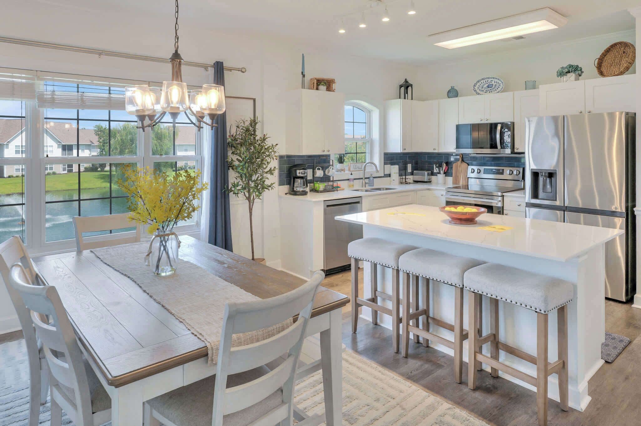 A modern kitchen with a central island, bar stools, and a dining area with a table and chairs.
