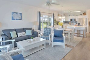 A modern living room with a sofa, coffee table, and chairs. There is a kitchen in the background with a refrigerator and a dining area. - Updated Large 2BR in Azalea Lakes, Pools, PondView (Myrtle Beach)