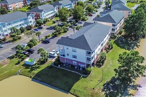 An aerial view of a residential area with multiple two-story buildings, a parking lot, and a small body of water.