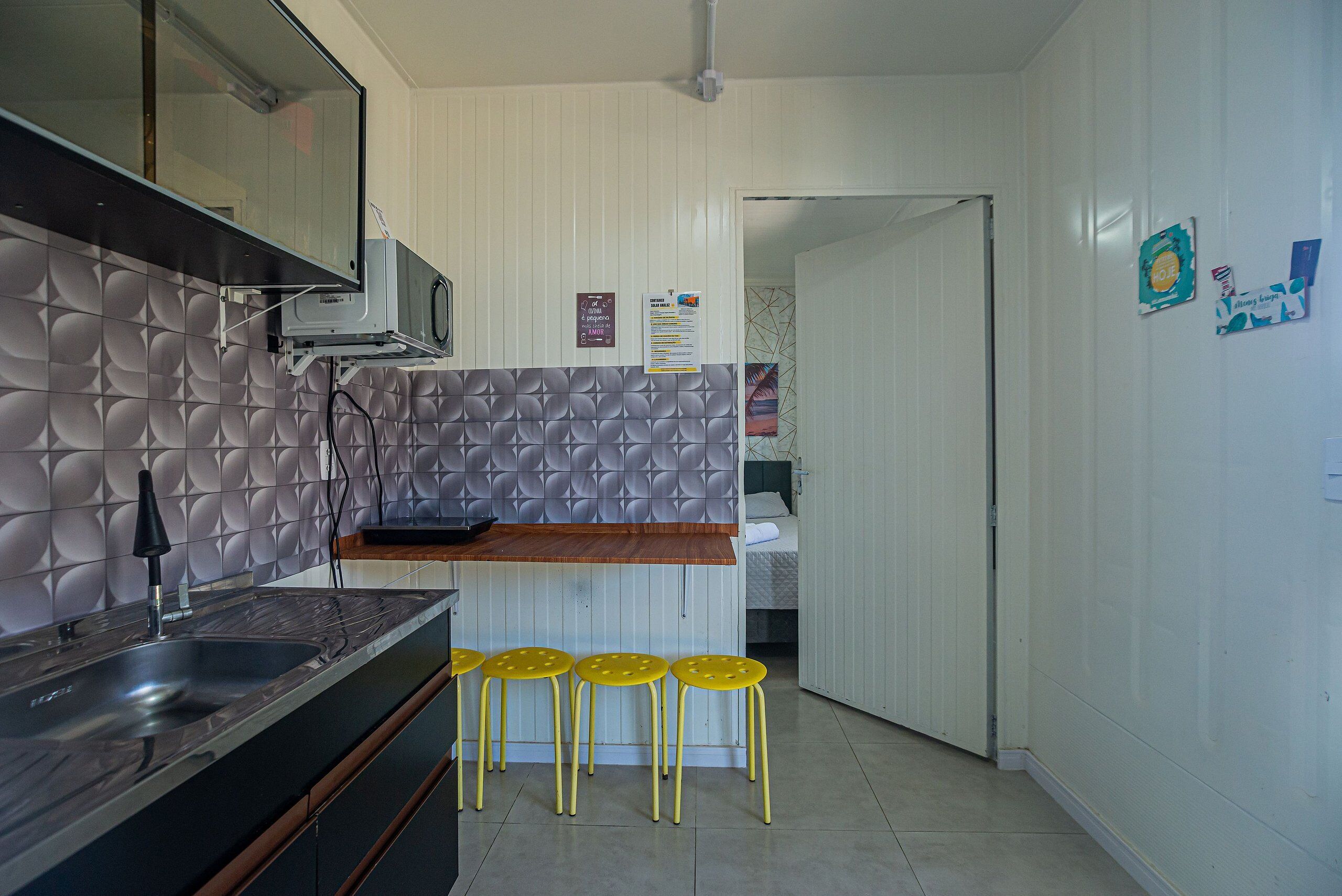 Una cucina con un lavandino, quattro sgabelli gialli, un forno a microonde e una porta bianca che dà su un'altra stanza.