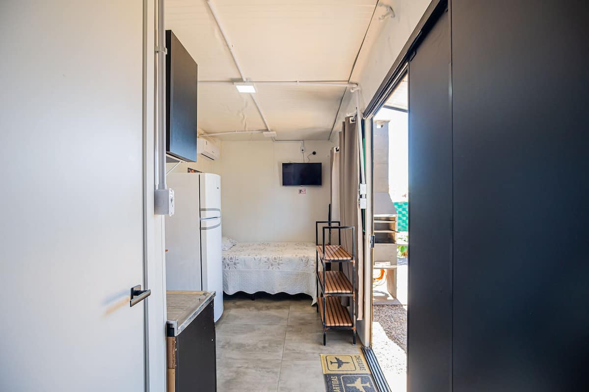 A narrow hallway with a bed, a television, and a shelf unit.