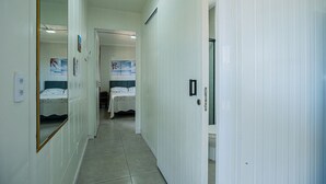 A narrow hallway with white walls and a tiled floor leading to a bedroom with a bed and a poster on the wall. - Container Beira Mar Solar Analuz (Navegantes)