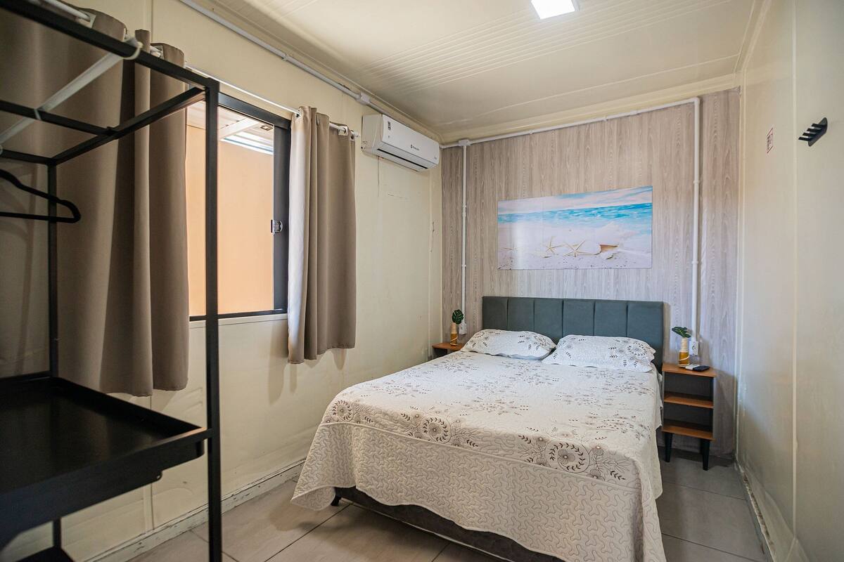 A bedroom with a bed, a nightstand, a wall-mounted air conditioner, and a window with curtains.