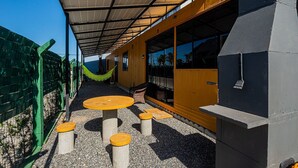 A covered outdoor seating area with tables and stools, a hammock, and a view of the ocean. - Container Beira Mar Solar Analuz (Navegantes)