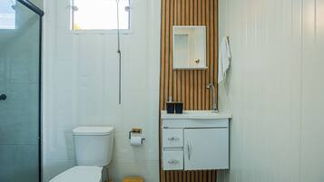 A bathroom with a toilet, a sink, a mirror, and a shower.