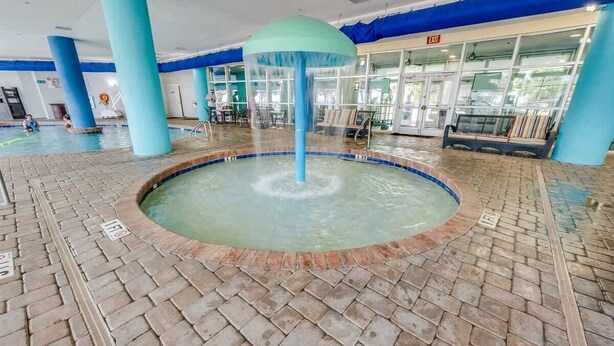A pool area with a central water feature, tiled flooring, and blue pillars. - Spacious City View - Close to Boardwalk, Location! (Myrtle Beach)