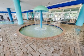 A pool area with a central water feature, tiled flooring, and blue pillars. - Spacious City View - Close to Boardwalk, Location! (Myrtle Beach)