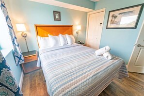 A neatly made bed with a striped blanket, a wooden headboard, and two bedside lamps. - Spacious City View - Close to Boardwalk, Location! (Myrtle Beach)