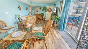 A dining area with a glass table, wicker chairs, and a view of the balcony. - Spacious City View - Close to Boardwalk, Location! (Myrtle Beach)