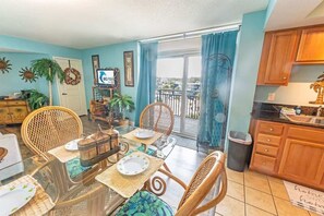 A dining area with a glass table, wicker chairs, and a view of the balcony. - Spacious City View - Close to Boardwalk, Location! (Myrtle Beach)