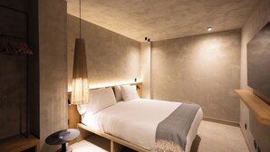 A modern bedroom with a bed, bedside table, lamp, and a hanging light fixture.