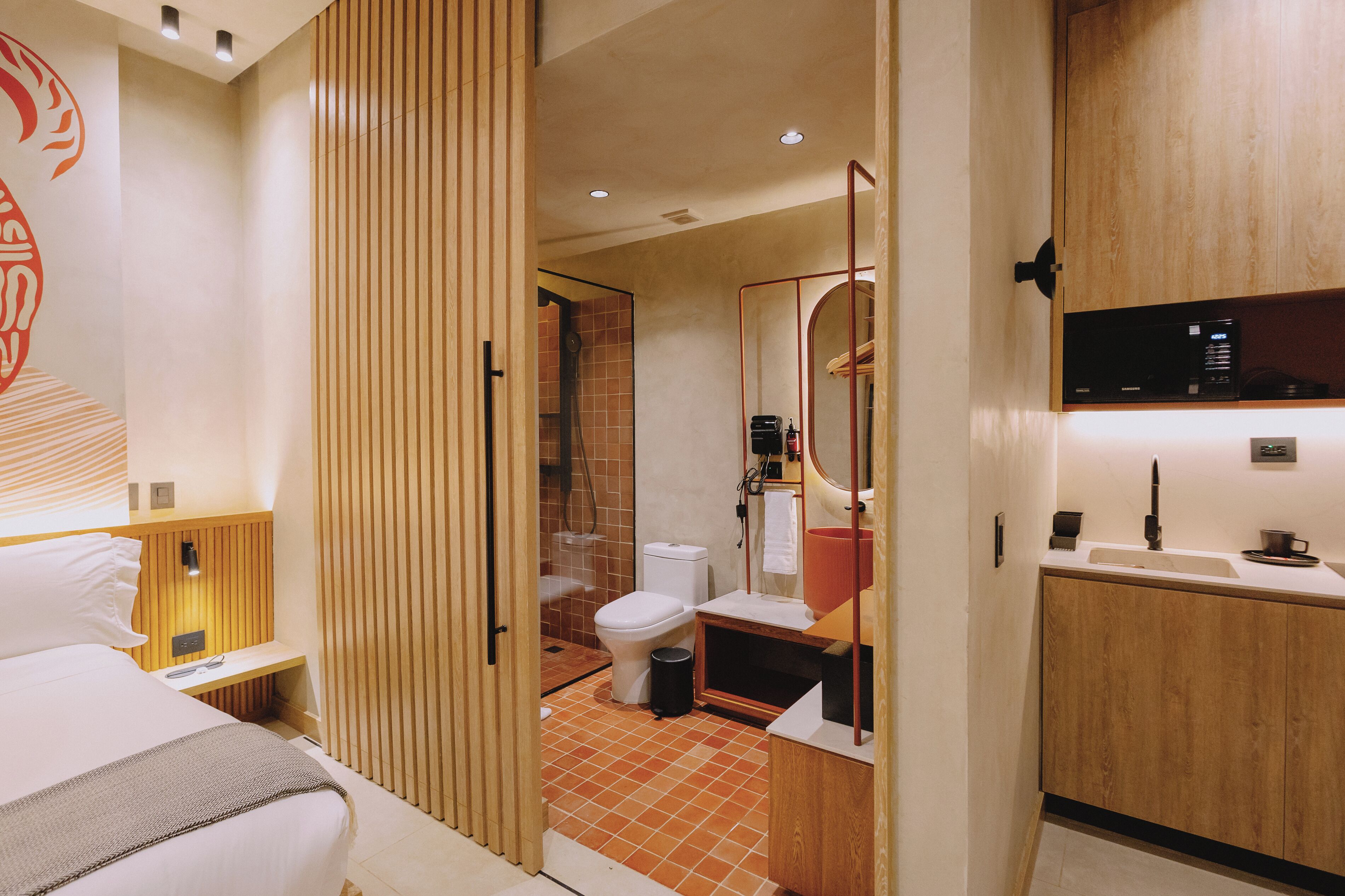 Ein modernes Hotelzimmer mit Bett, einer Holzwand, einer Duschkabine, einer Toilette und einer kleinen Küchenzeile.