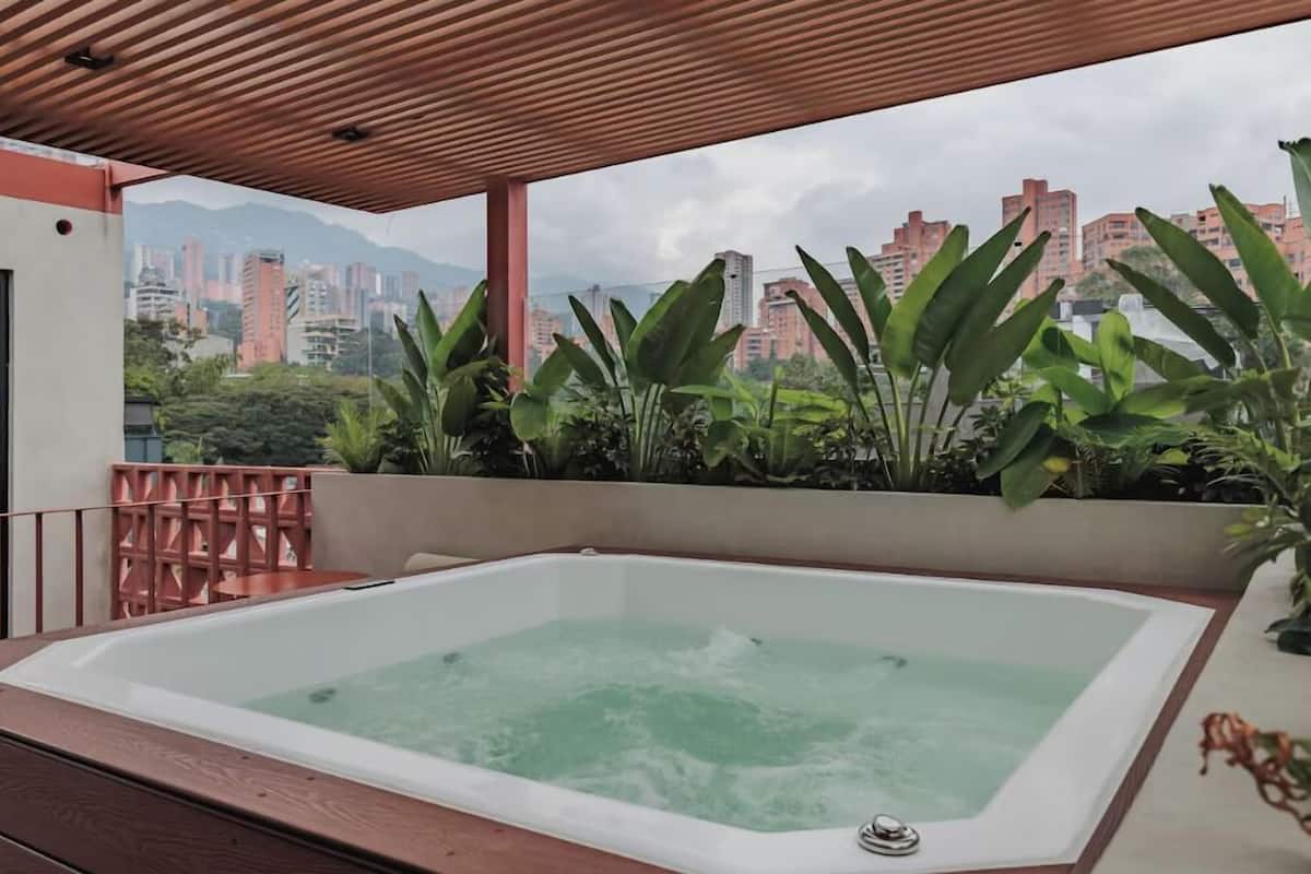 A hot tub with a cityscape view, surrounded by lush greenery.