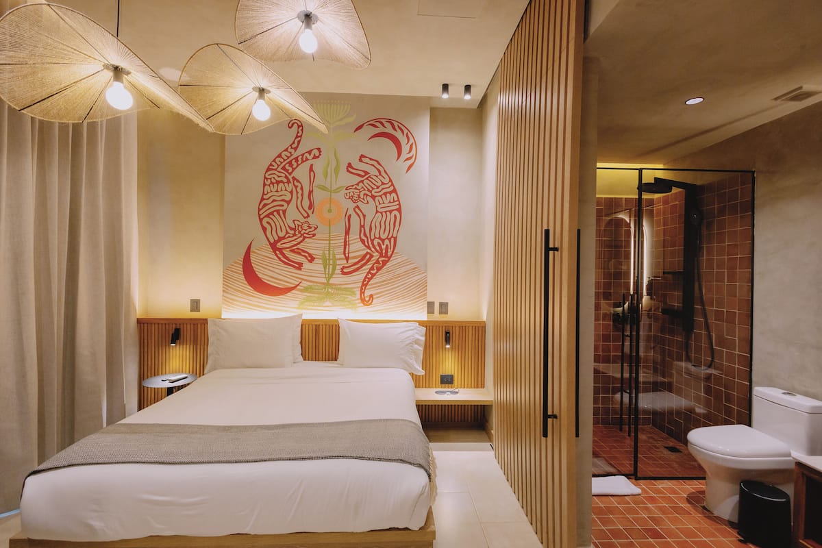 A hotel room with a large bed, bedside tables, a wall mural, and a separate bathroom with a shower and toilet.