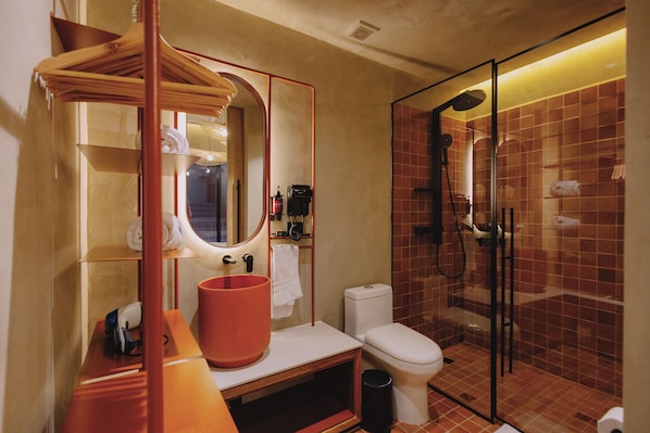 Un baño moderno con ducha envuelta en vidrio, un lavamanos blanco con un lavabo rojo y un espejo con marco de madera.