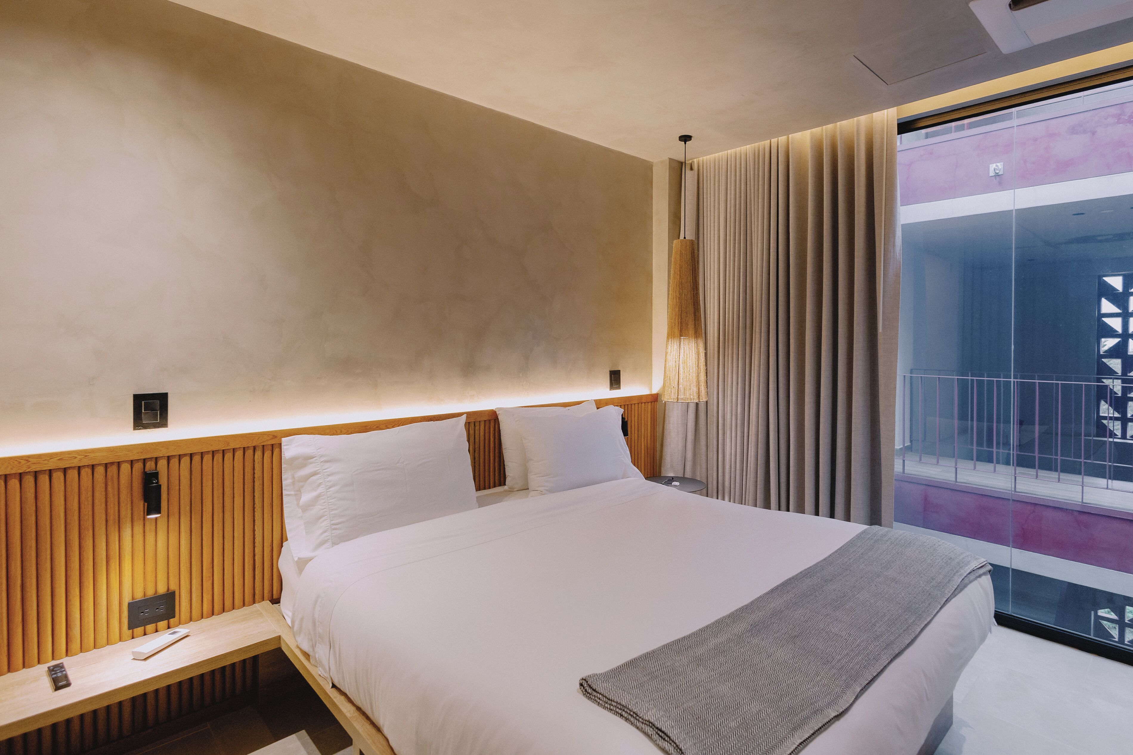 Una habitación de hotel con cama, mesita de noche y ventana con cortinas.