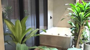 A modern bathroom with a bathtub, large potted plants, and a wooden ceiling.