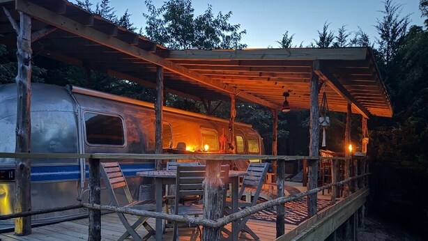 A rustic wooden deck with a covered seating area and a vintage camper van. - Deluxe camping in newly remodeled airstream! (honey Grove)