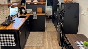 A compact kitchen with a wooden countertop, a sink, and a small dining area with a table and chairs. - Deluxe camping in newly remodeled airstream! (honey Grove)