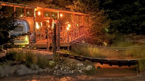 A rustic wooden structure with a metal roof, surrounded by trees and a gravel path. - Deluxe camping in newly remodeled airstream! (honey Grove)