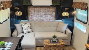A cozy interior with a sofa, a small table, and a wicker coffee table. - Deluxe camping in newly remodeled airstream! (honey Grove)