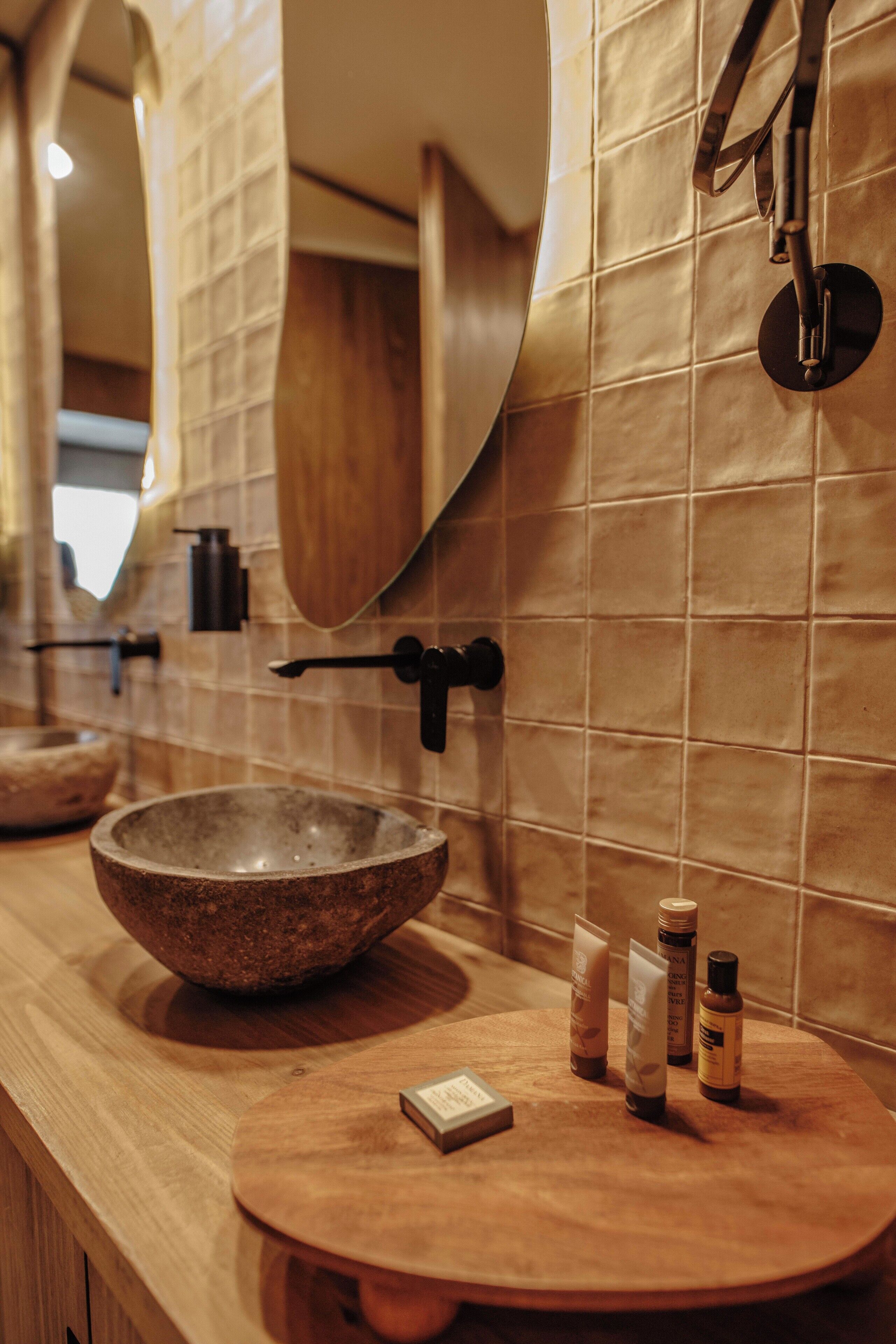 A bathroom with a large stone basin, wooden vanity, and tiled walls.