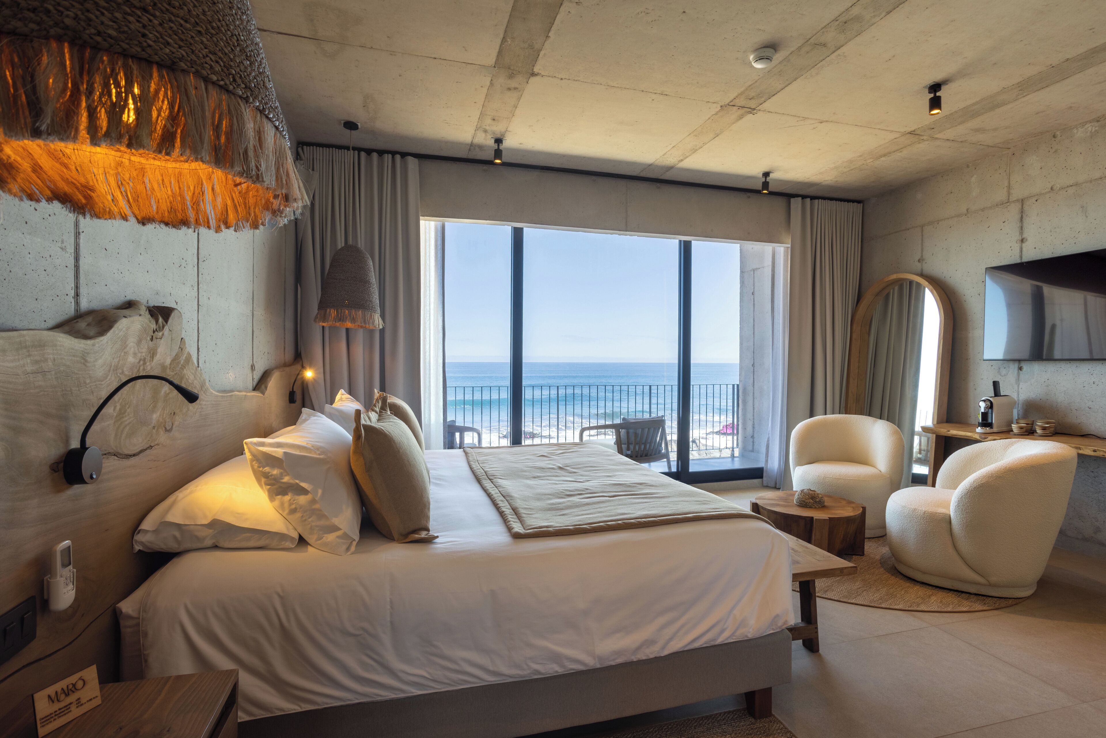 Una habitación de hotel moderna con una cama grande, vista a la playa y un balcón.