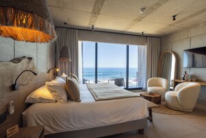 Una habitación de hotel moderna con una cama grande, vista a la playa y un balcón.