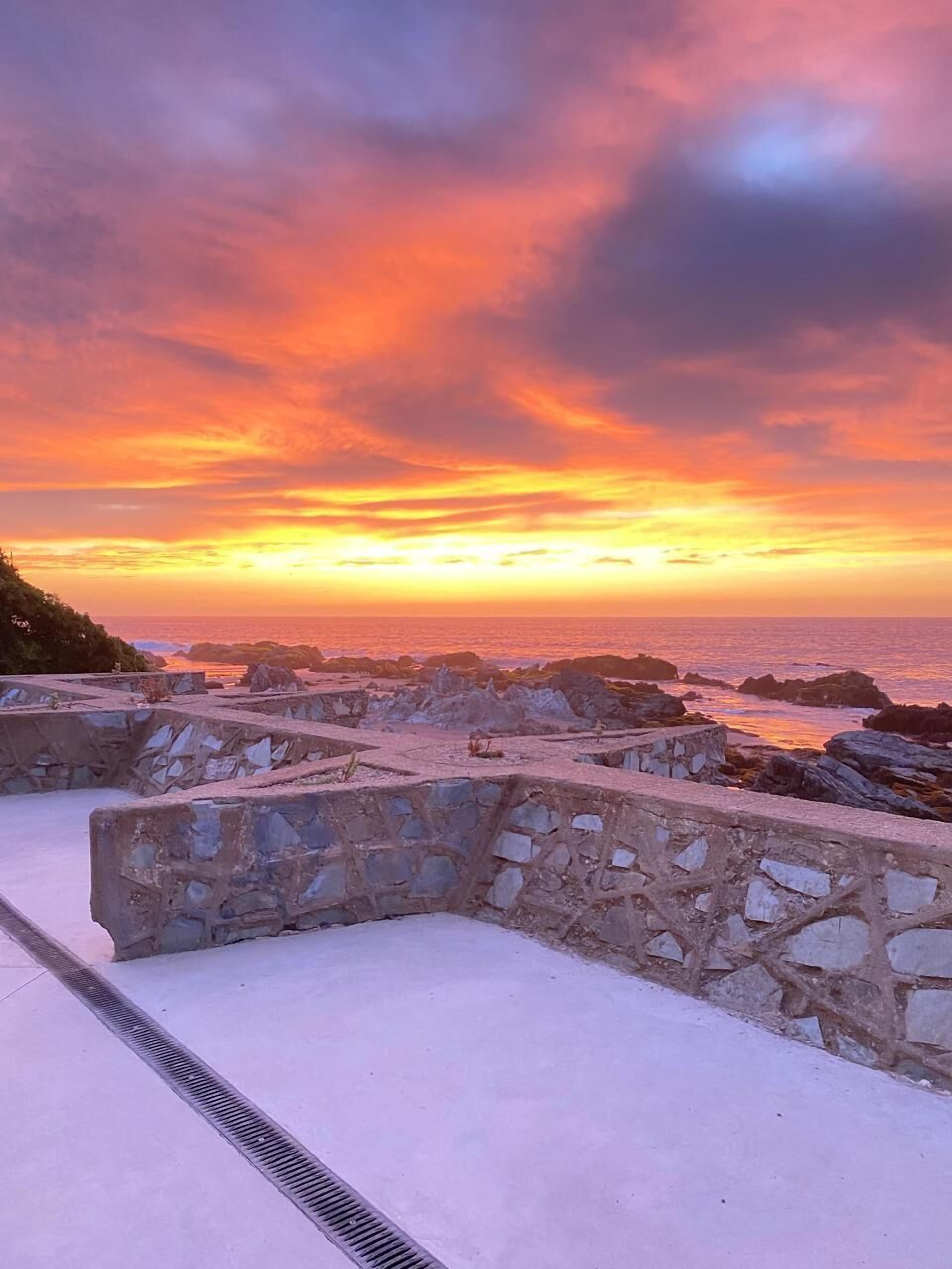 A stone pathway leading to a beach with a sunset view.
