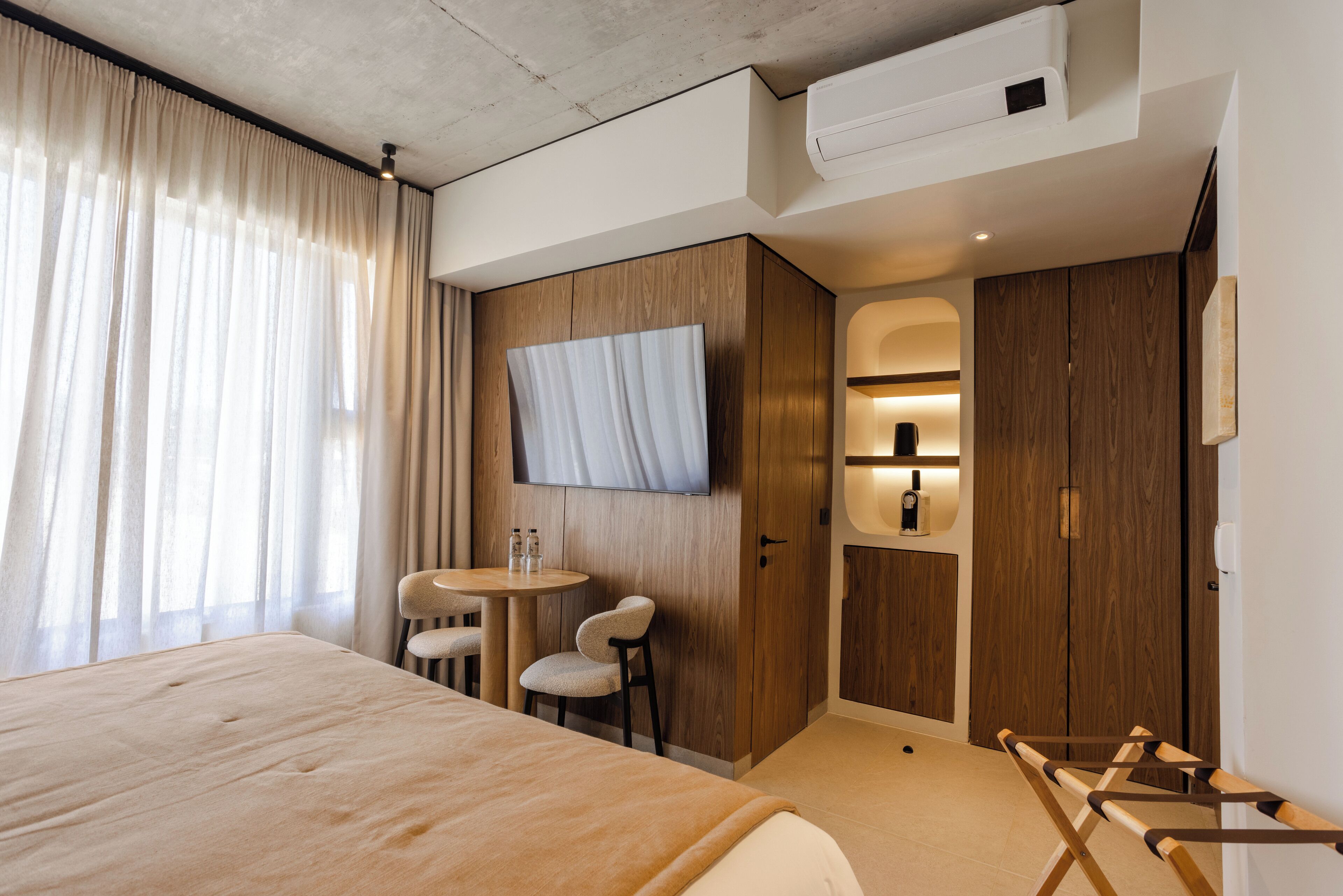 A hotel room with a large bed, a TV mounted on the wall, a small round table with two chairs, and wooden wardrobes.