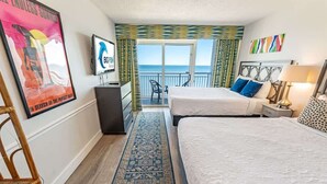 A hotel room with two beds, a TV, a desk, and a view of the ocean. - 1BR Camelot Resort, Direct Oceanfront Views,Pools! (Myrtle Beach)
