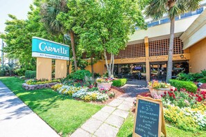 A hotel entrance with a sign for 'The Caravelle,' a paved pathway, and a flower bed.