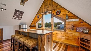 A cozy kitchen with a wooden bar, a refrigerator, and a window with a view of the outside.