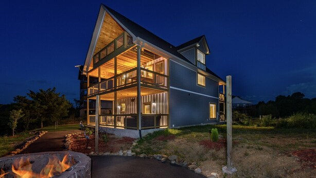 A two-story house with a stone fire pit in the foreground.